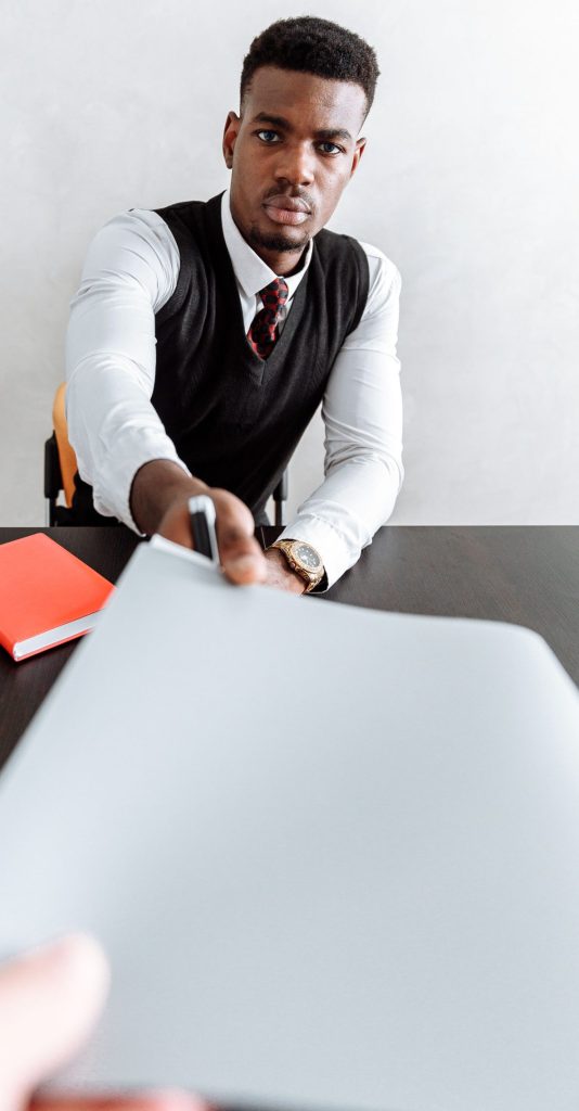 Man handing a CV over a table to another.